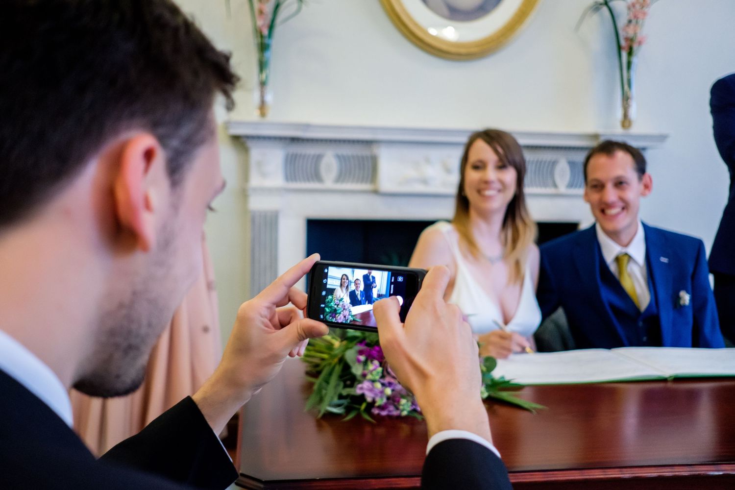 Wedding guests gather indoors near decorative white walls and architectural details.