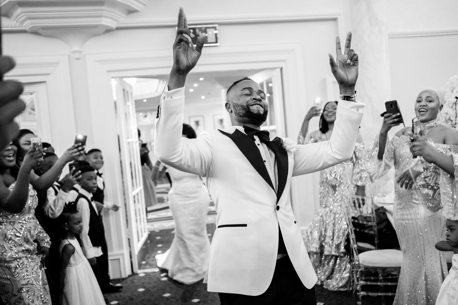 Black and white photo of wedding guests celebrating energetically on a packed dance floor.