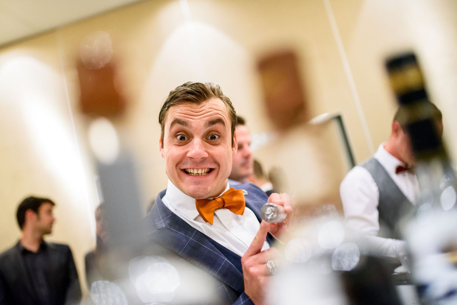 A smiling person in a navy suit and orange bow tie poses enthusiastically at a formal event.