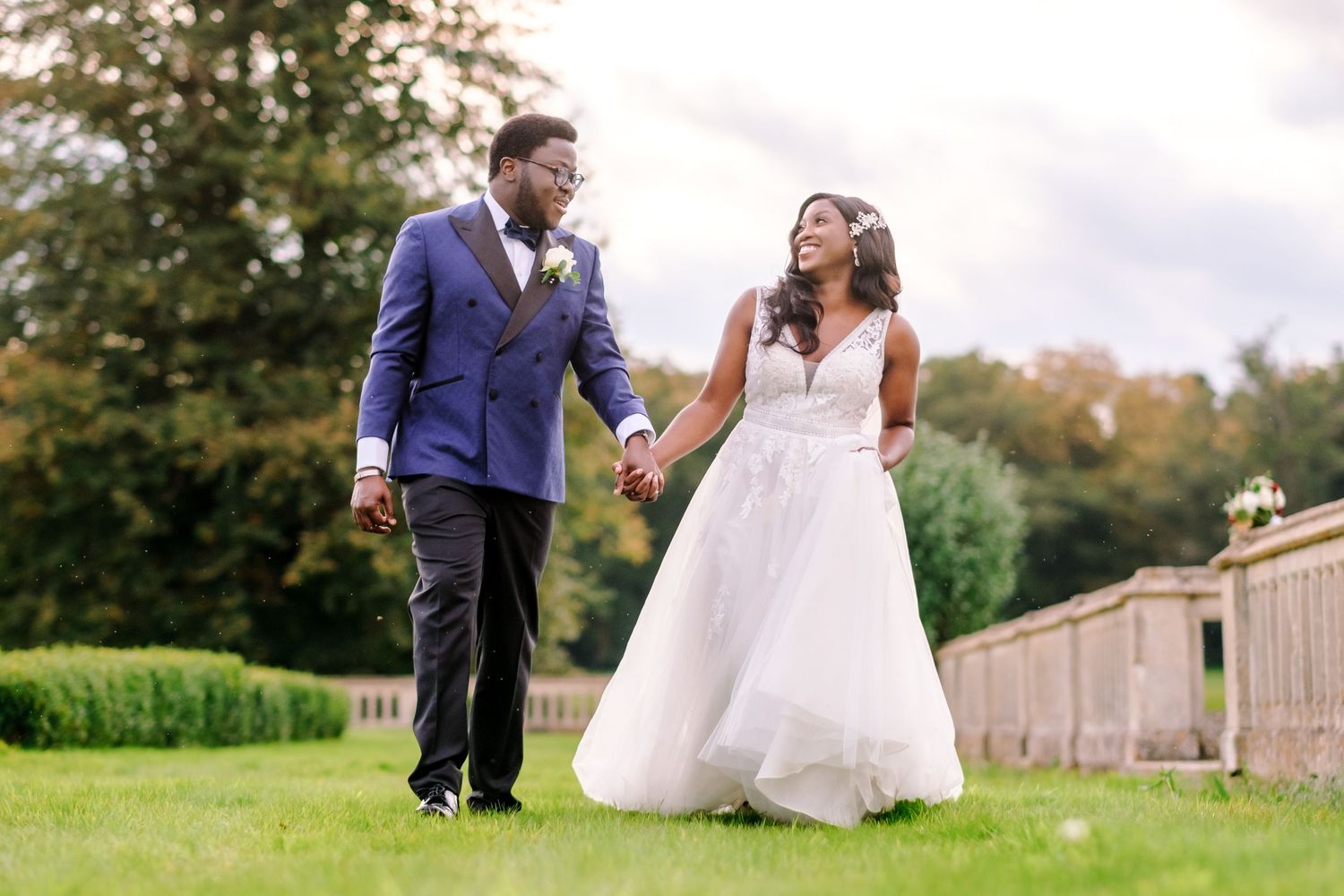 Couple walking together on the grounds of a historic estate surrounded by green lawns and gardens.
