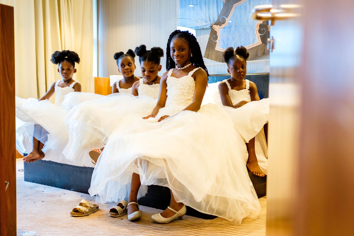 A group of people in white clothing relax on a couch in a warmly lit room with wooden accents.