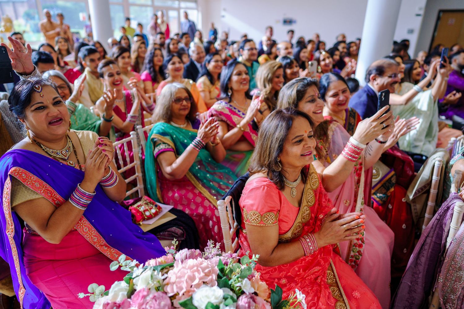 Wedding guests in vibrant saris clapping and celebrating during an Indian wedding celebration.