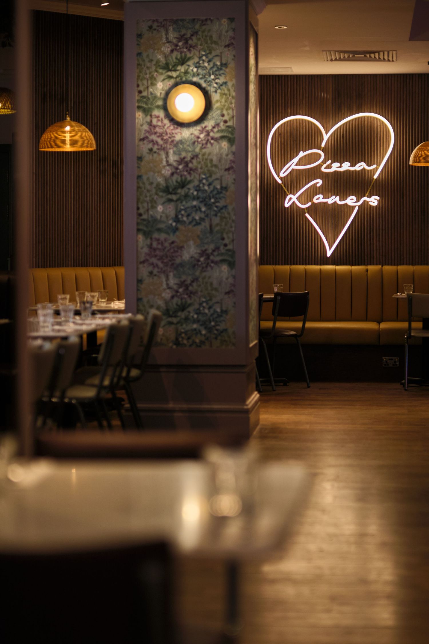 Modern restaurant interior with neon heart sign and floral wallpaper creating a romantic ambiance.