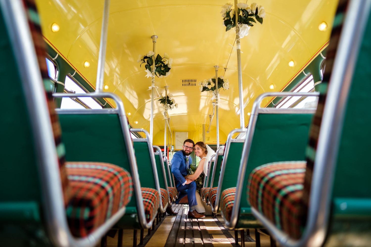 Wedding party poses inside a vintage train car with yellow ceiling and green seats.
