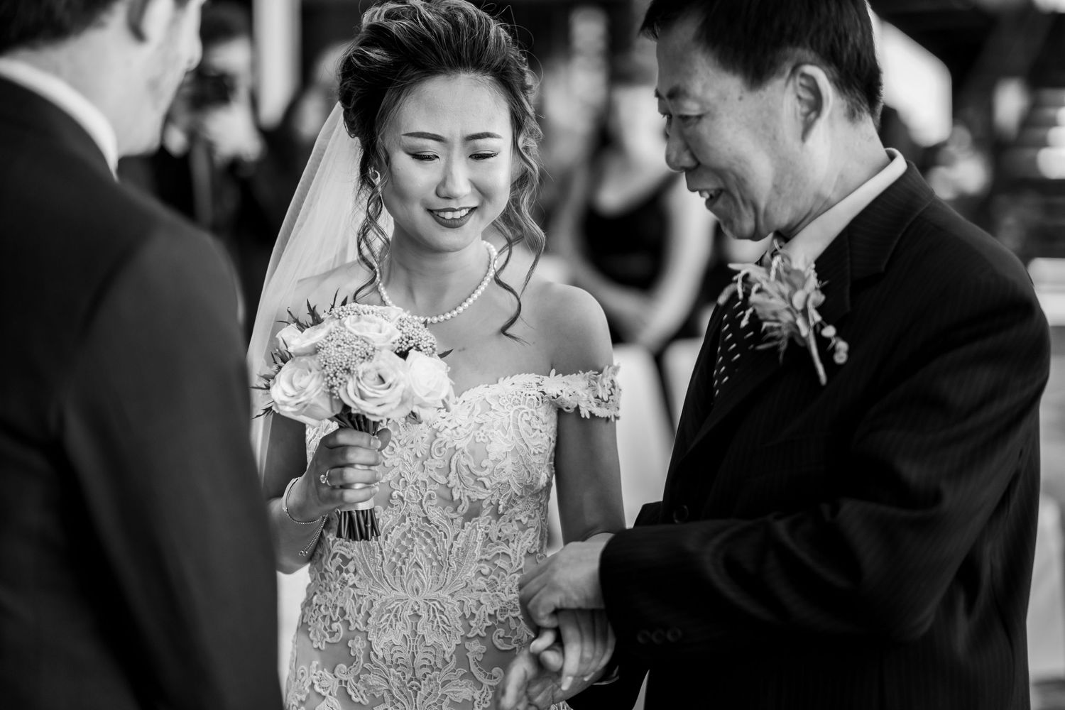 A joyful bride in a lace off-shoulder gown shares a tender moment with a guest during her wedding ceremony.