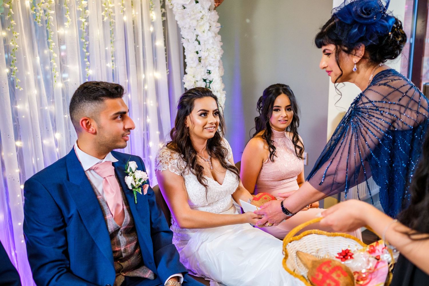 Wedding party dancing and celebrating in a reception hall decorated with string lights and purple uplighting.