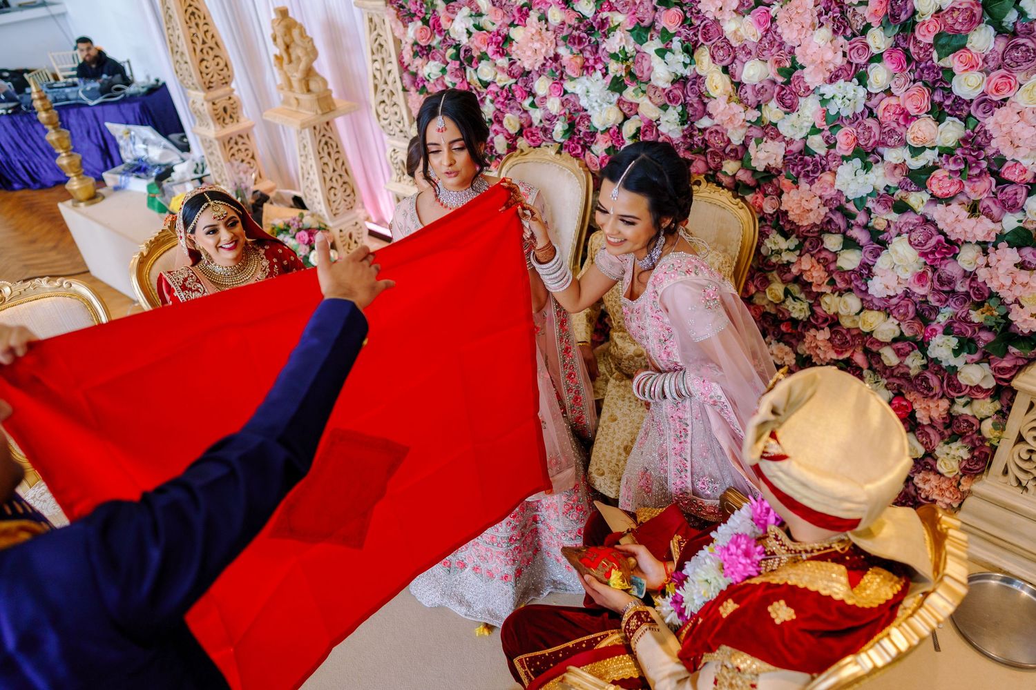 Traditional Indian wedding ceremony with red dupatta being held over decorative floral backdrop.