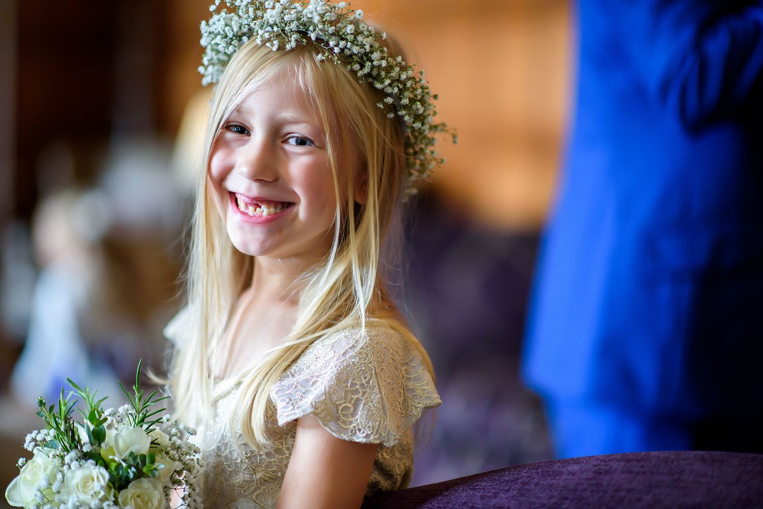 Young attendant smiles joyfully wearing a delicate flower crown at a wedding celebration.