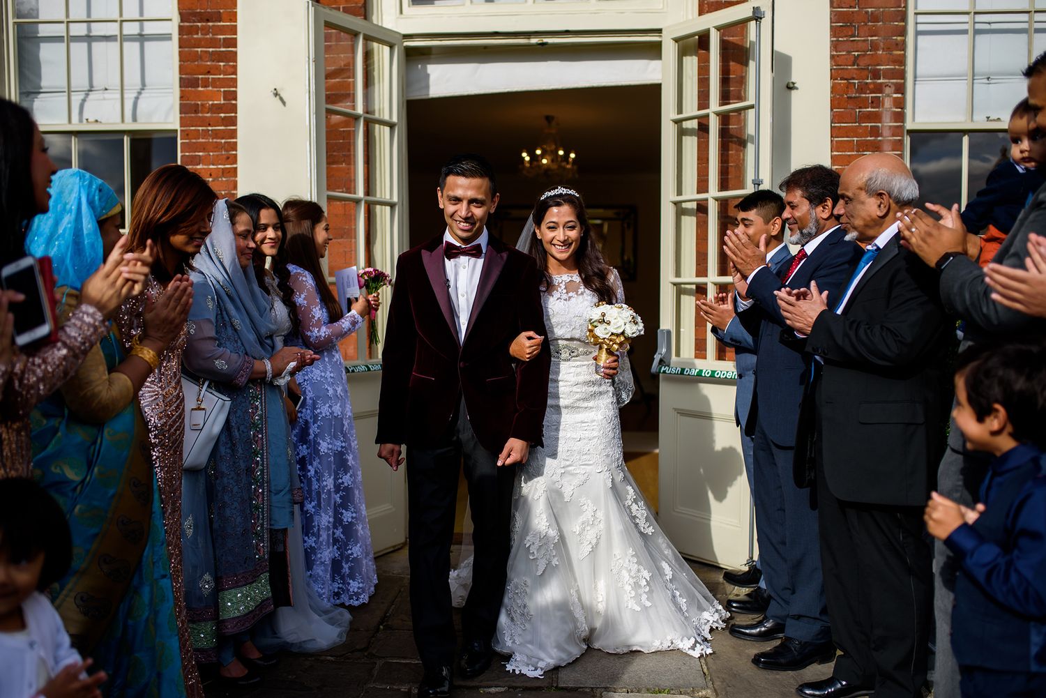 Wedding celebration along brick building exterior with guests watching.