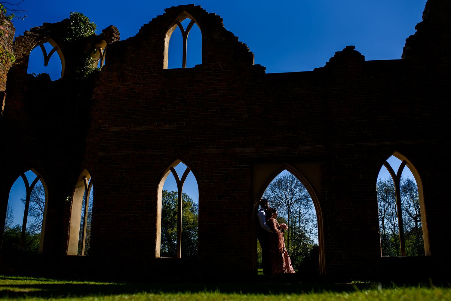 Ancient church ruins silhouetted against bright blue sky with Gothic arched windows.