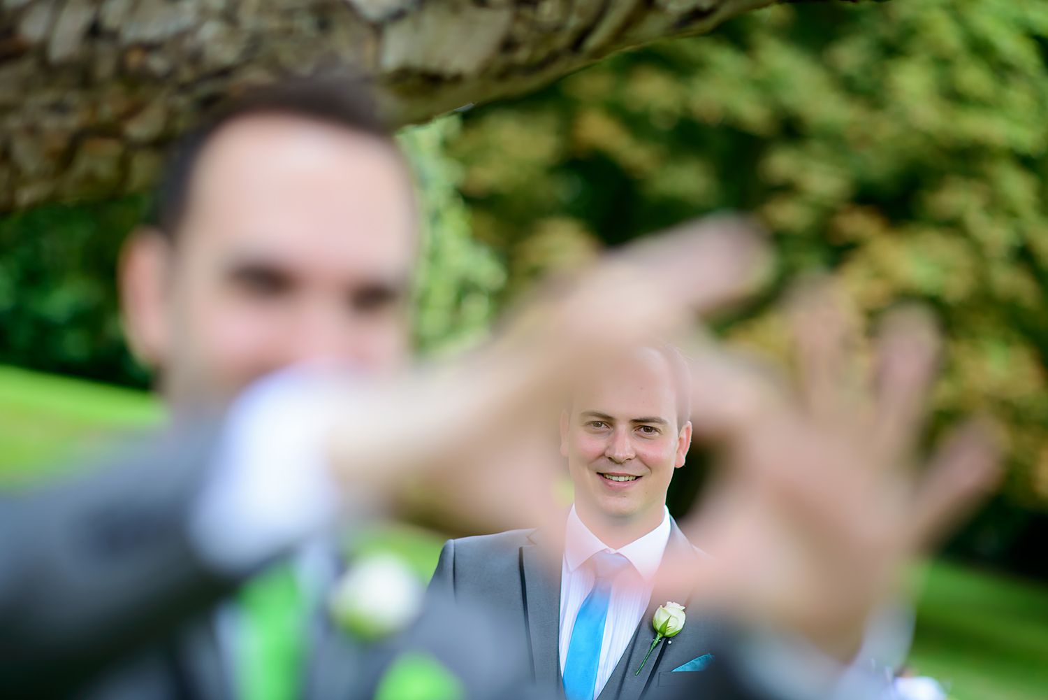 Playful portrait through fingers at outdoor wedding photoshoot.