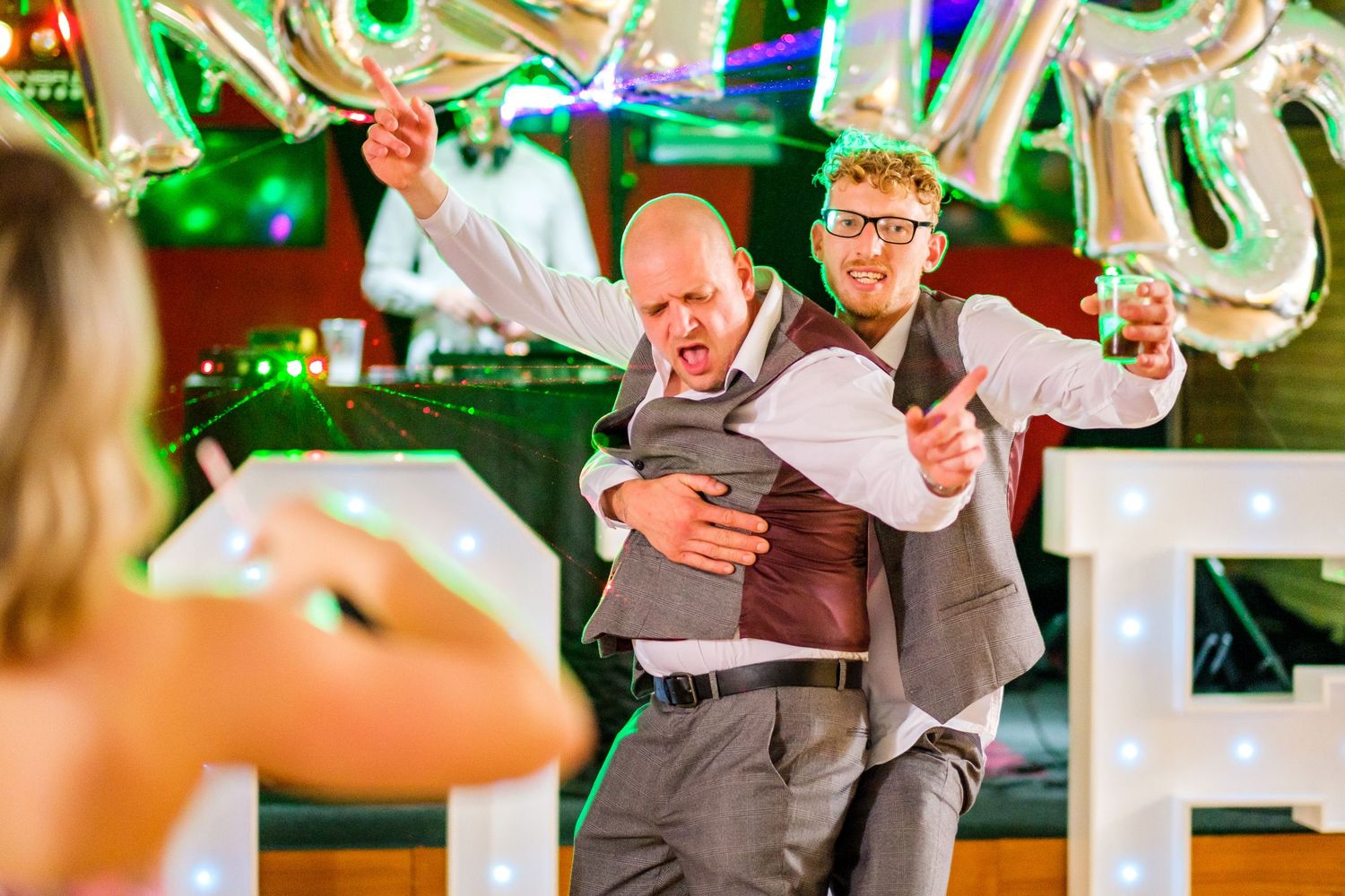 Wedding guests dancing and celebrating under green party lighting and decorations.
