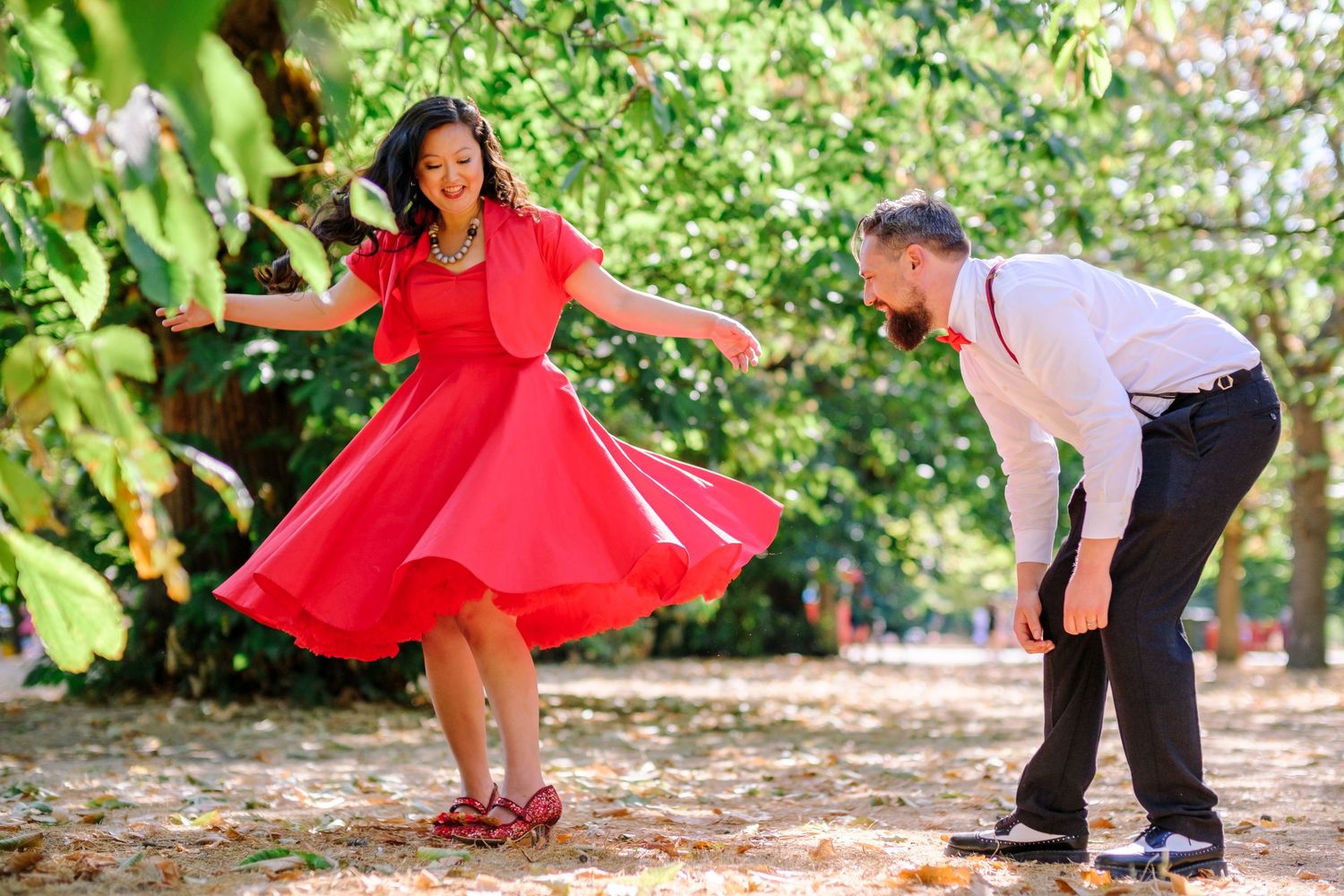 Dancers in red dresses and black outfits perform choreographed moves in a garden setting with lush greenery.