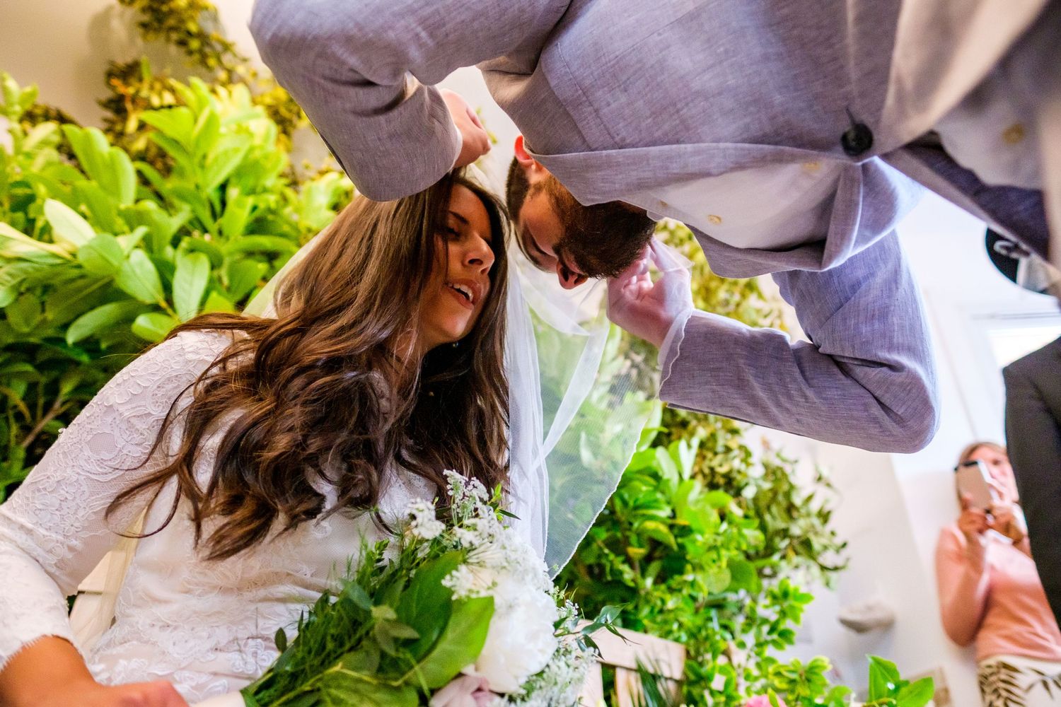 Two people in white and gray outfits inspect fresh herbs and vegetables growing in a garden setting.