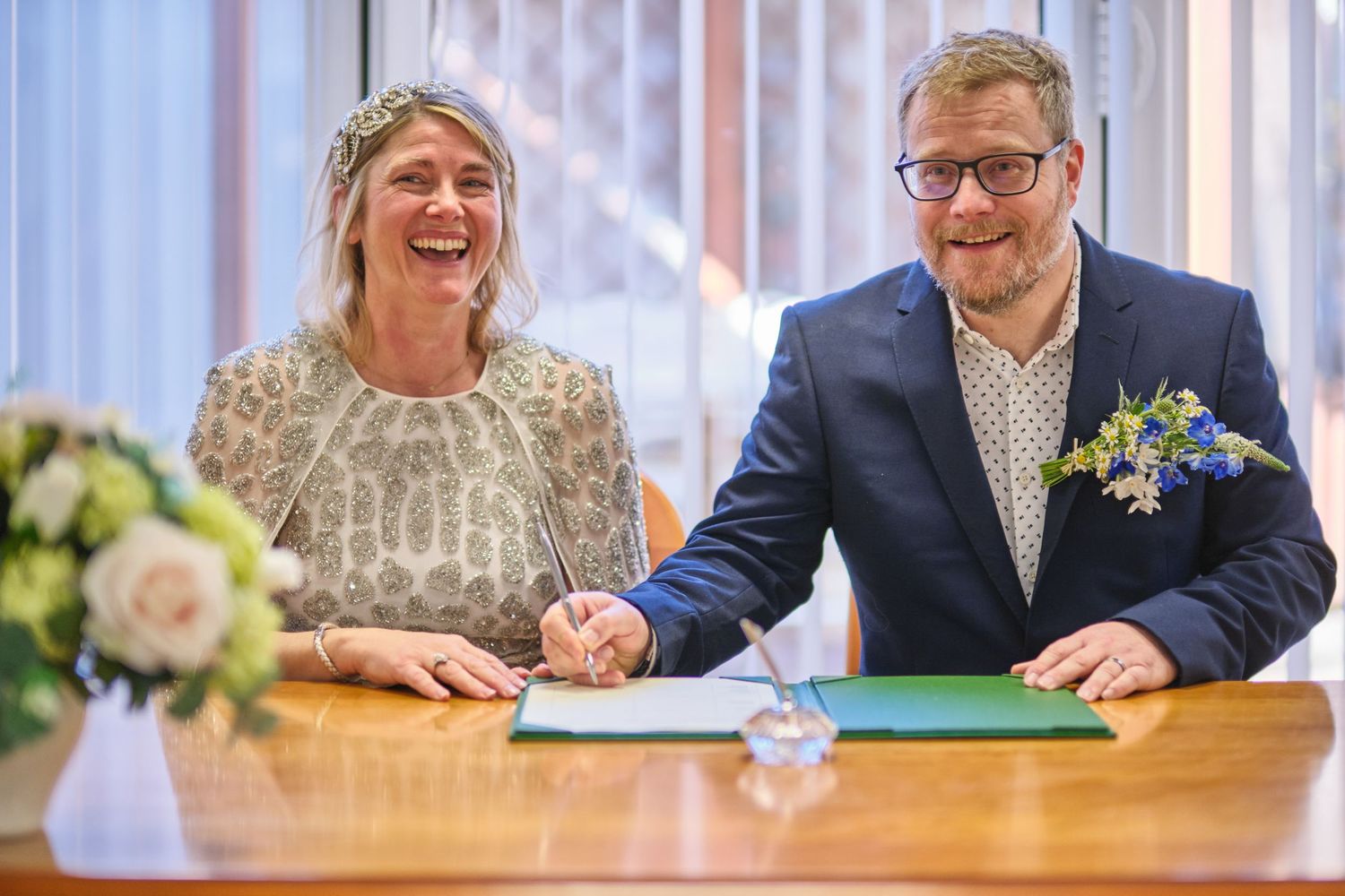 Couple signing documents at a wooden table during a civil ceremony.
