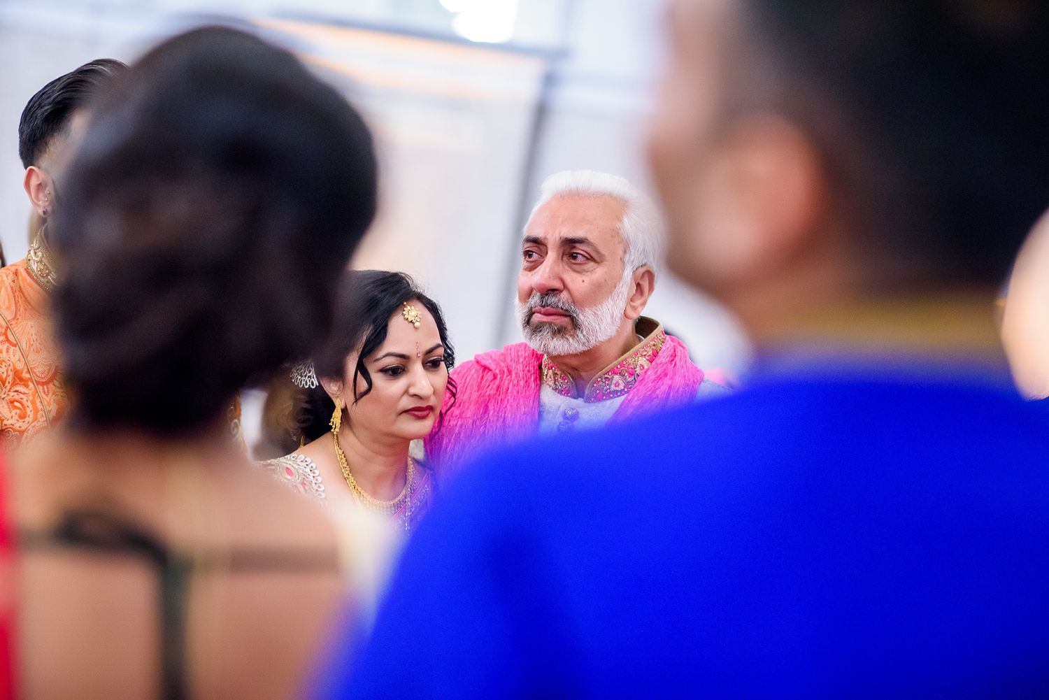 Wedding guests in formal attire seated during ceremony with blue lighting effects.