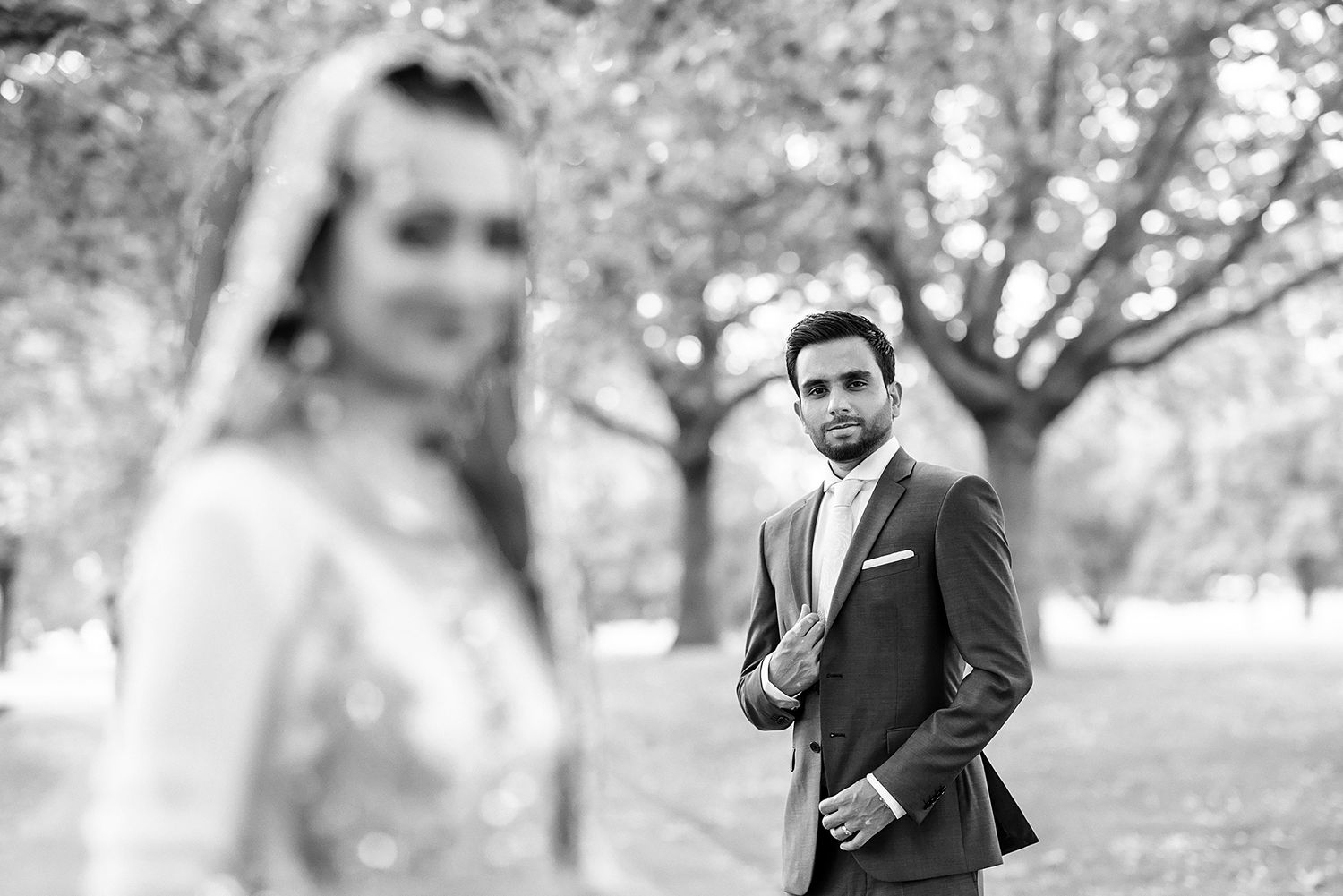 Black and white wedding portraits in a park setting with natural bokeh effect.