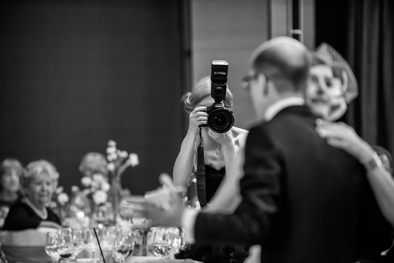 Black and white reception scene with guests mingling at tables with glassware.