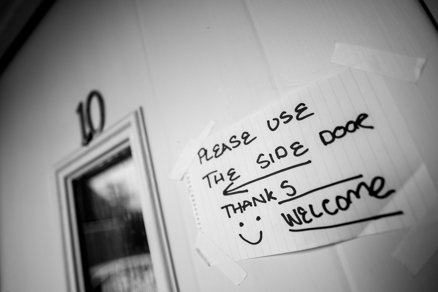 A handwritten note on a wall asking visitors to please use the side door with a smiley face.