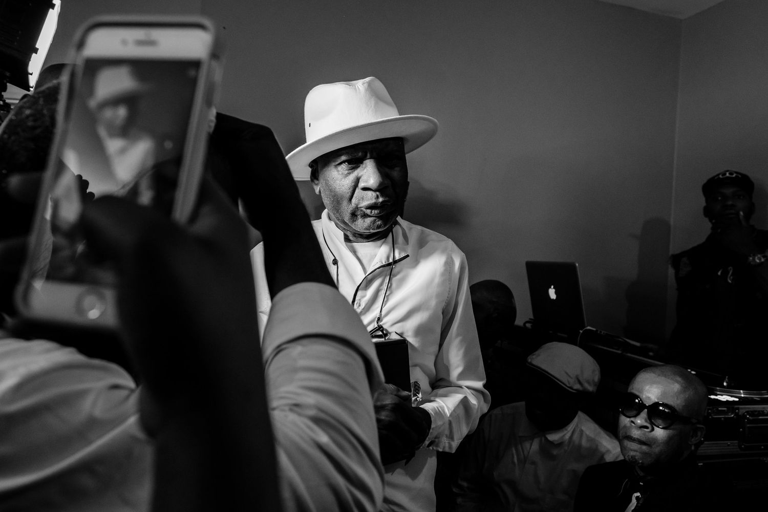 A person in a white hat being photographed by mobile phones in a dimly lit room.