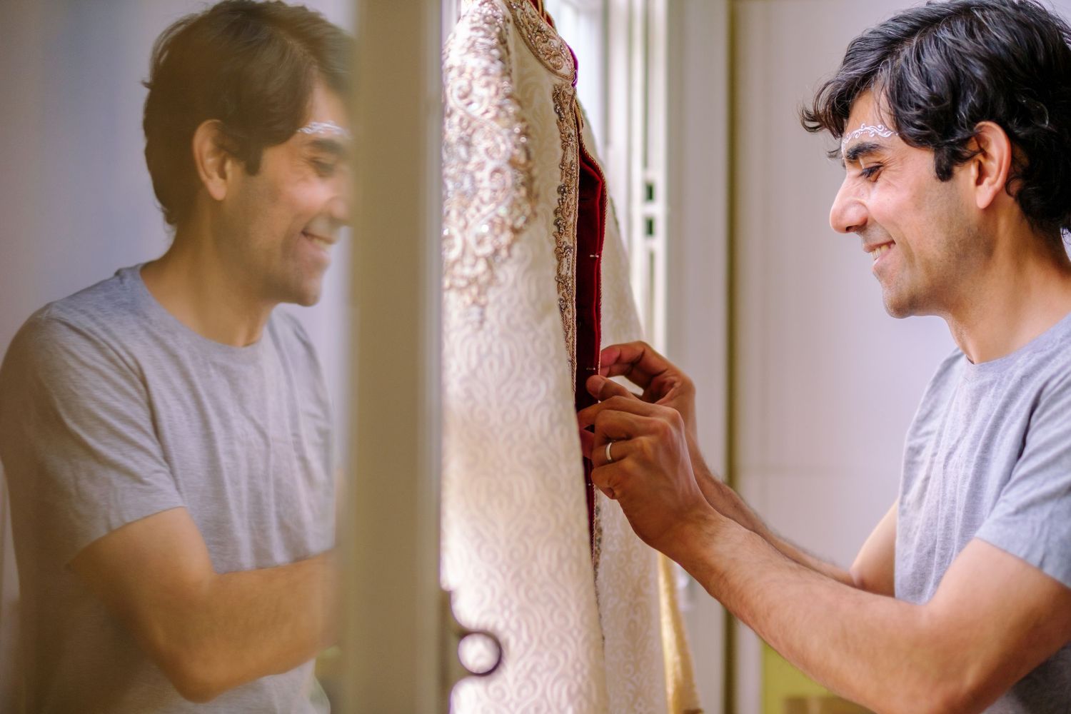 Man in white shirt smiling and gesturing while looking at smartphone screen in bright interior setting.
