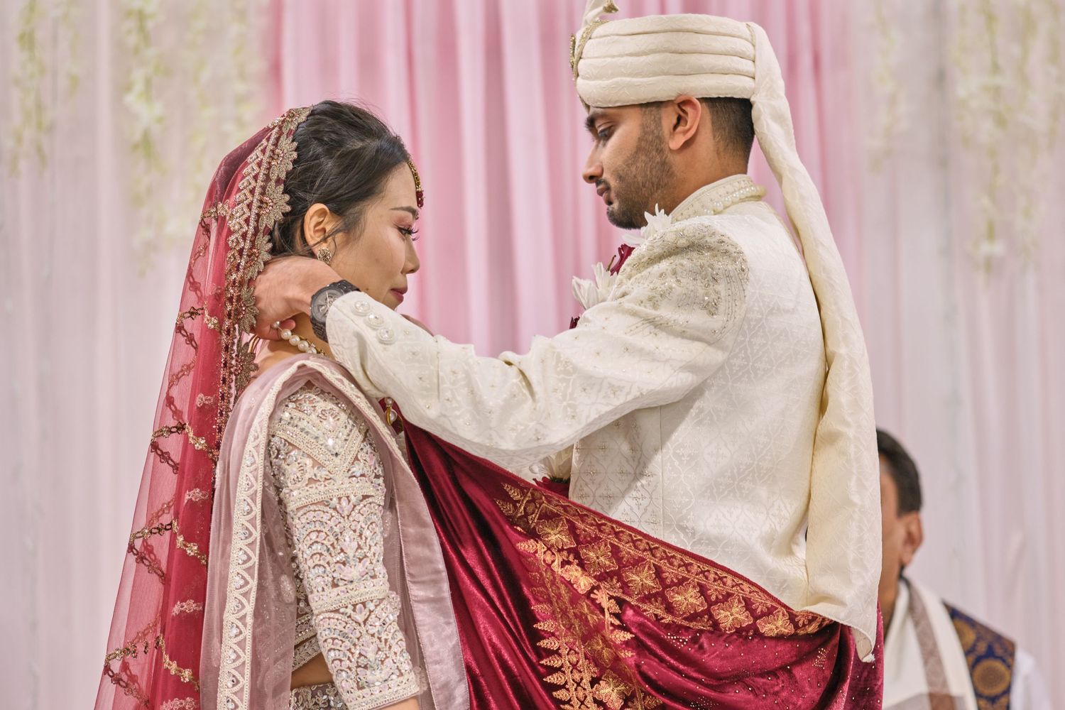Traditional Indian wedding ceremony with couple performing rituals under pink and white decorated mandap.