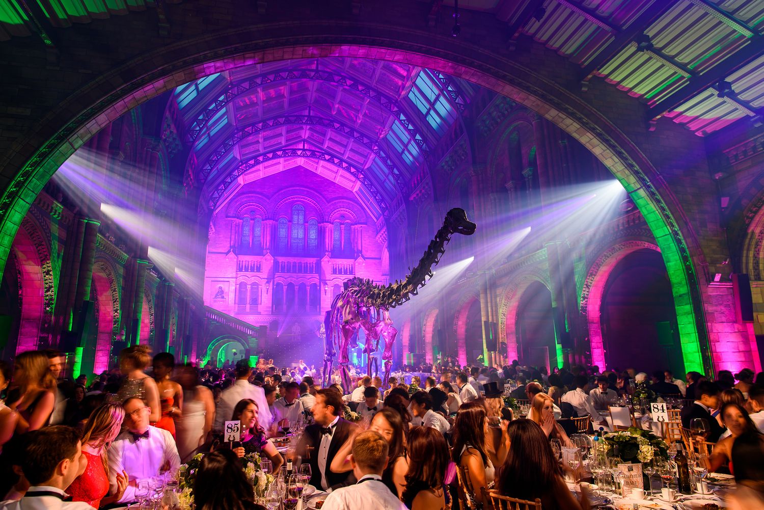 Large event space with purple and green lighting illuminating an arched ceiling structure.