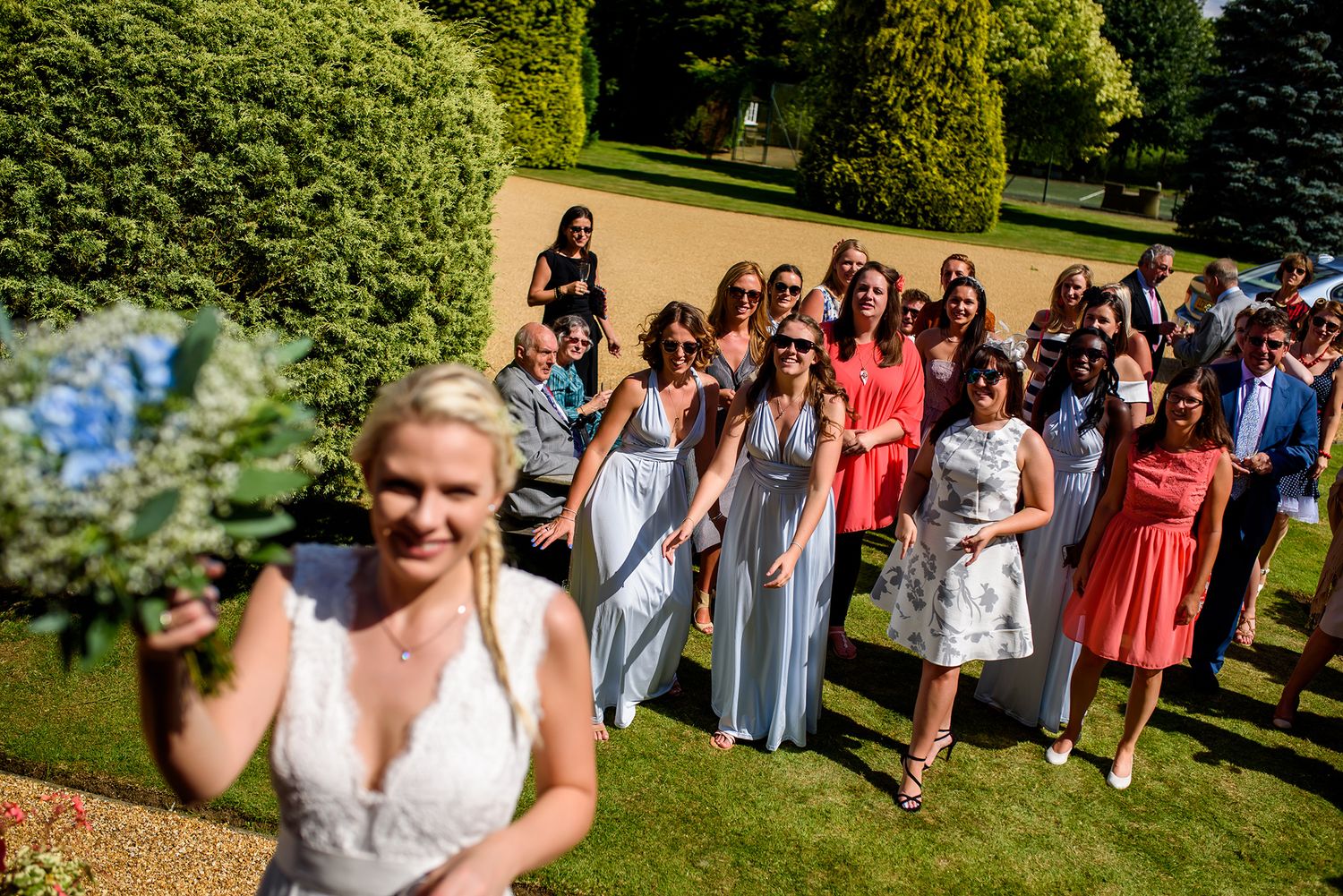 Large group of wedding attendees gathered on a sunny lawn for photos.