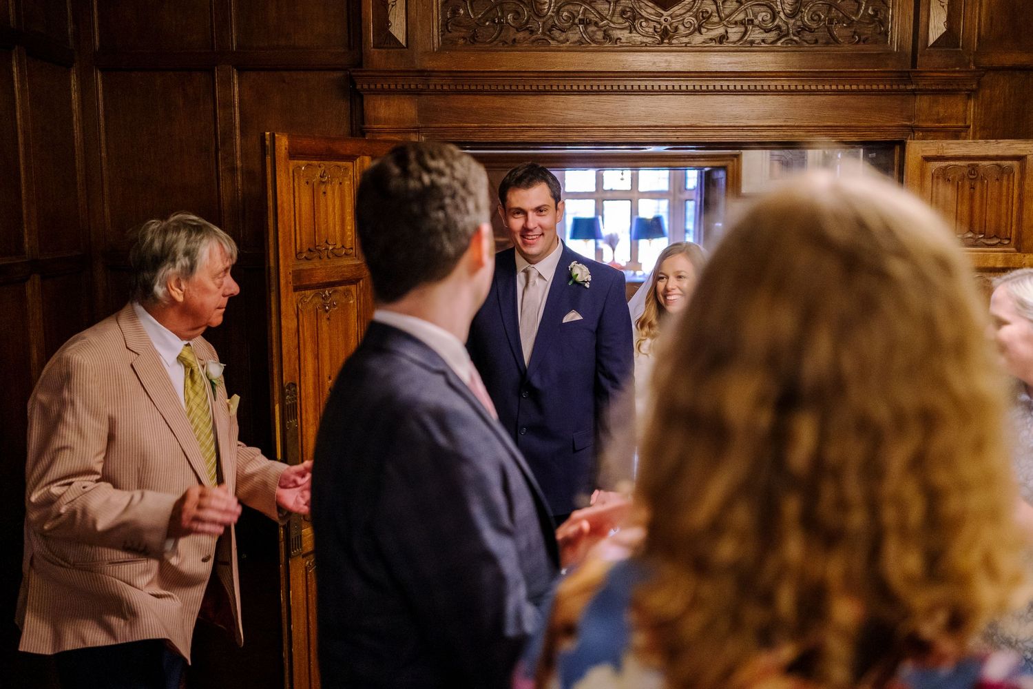 A group of people gathered in an elegant wood-paneled room with ornate decor and moldings.
