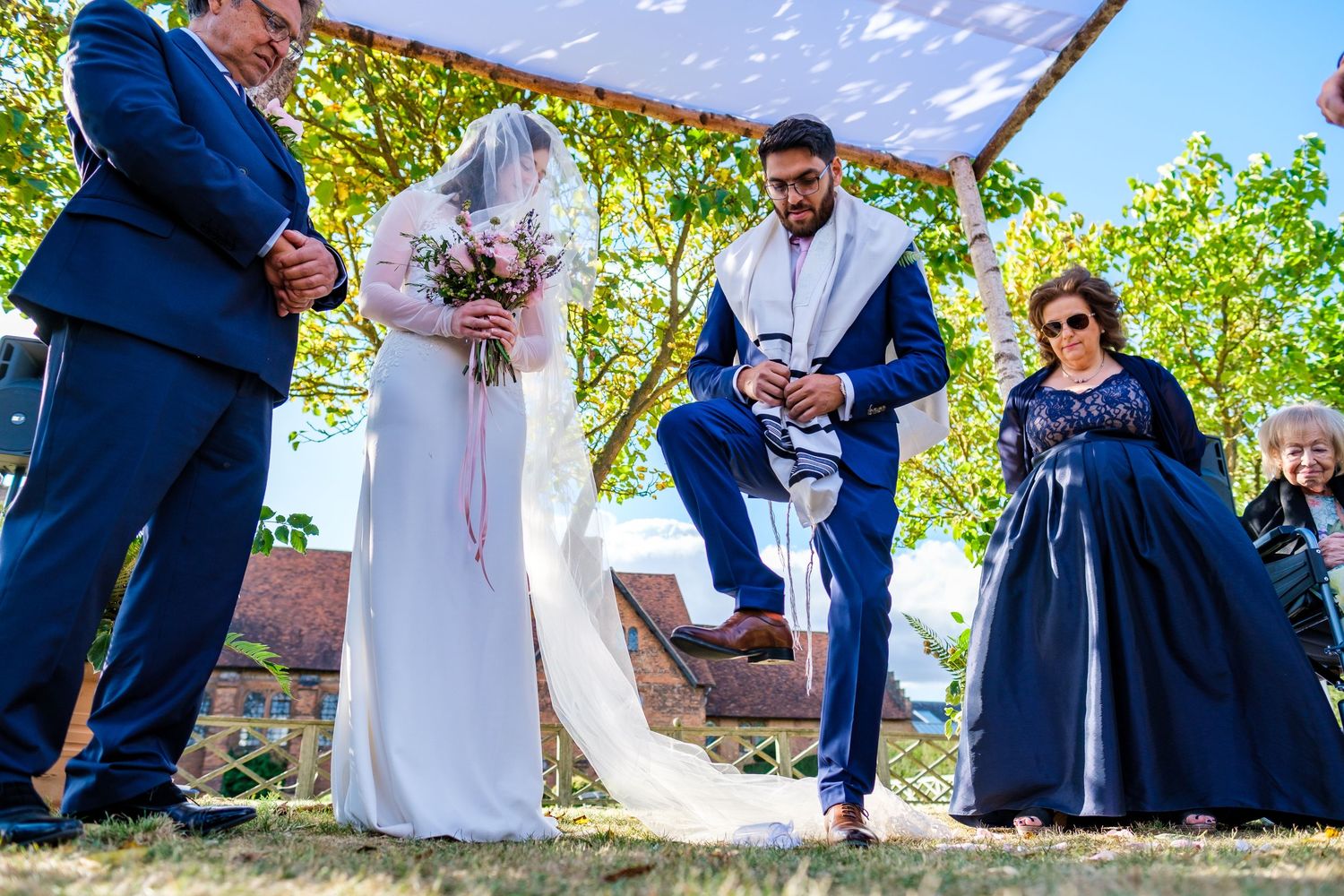 Wedding celebration outdoors with blue sky and green foliage backdrop.