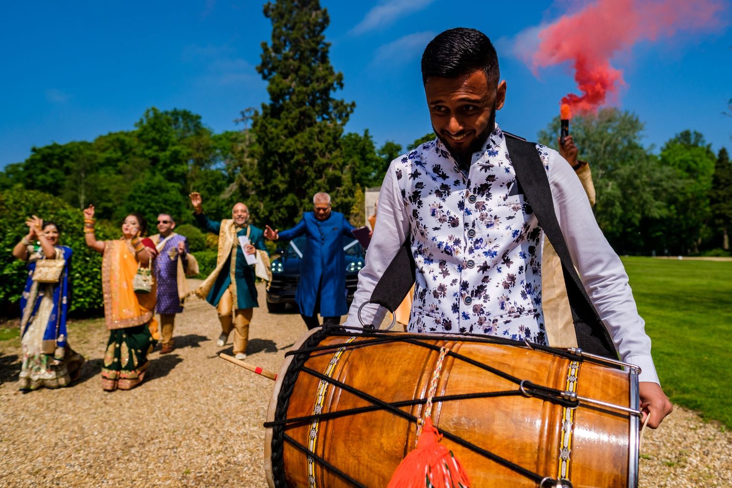 Celebratory group throws colorful smoke bombs outdoors against bright blue sky during festive gathering.