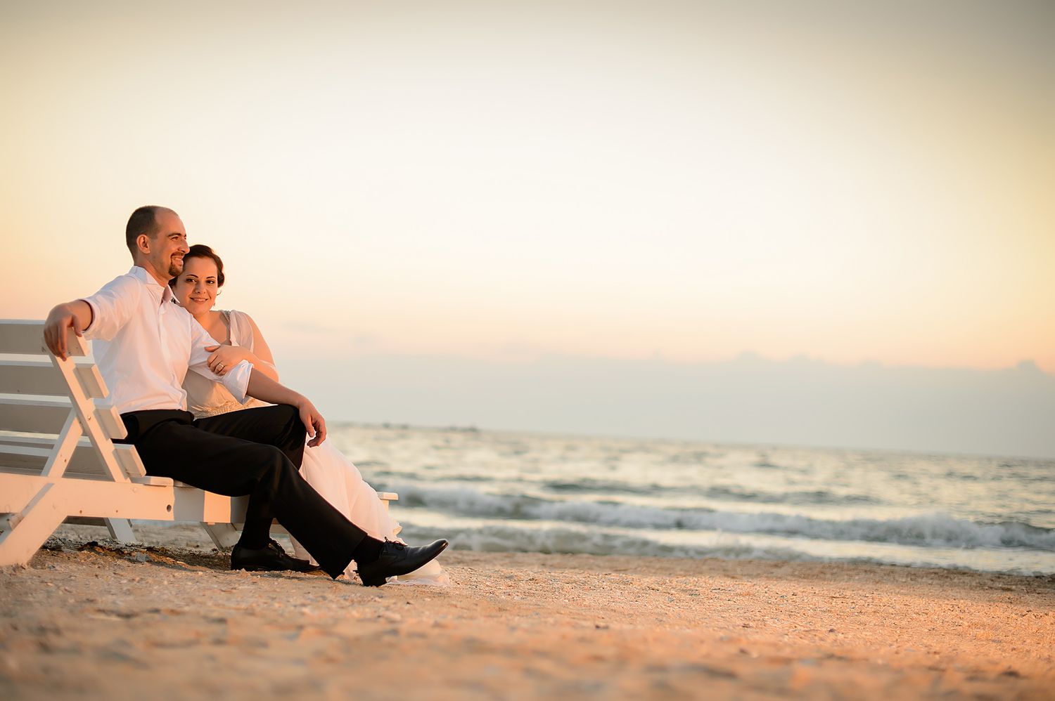 A romantic couple relaxes on a beach chair at sunset by the ocean waves.