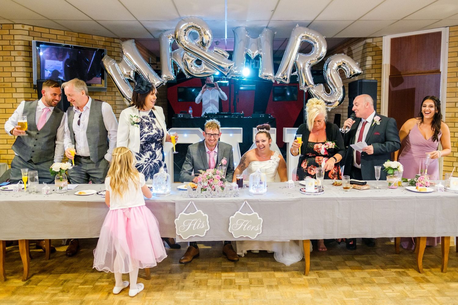 Long reception table decorated for wedding celebration with Mr and Mrs sign visible in background.