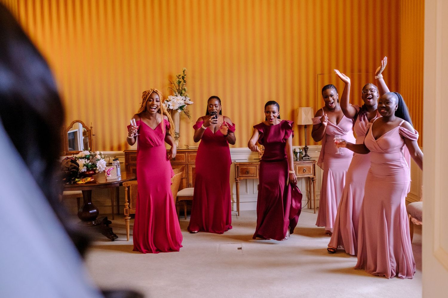 Wedding party in pink and red dresses dancing and celebrating in an elegant indoor venue with warm lighting.