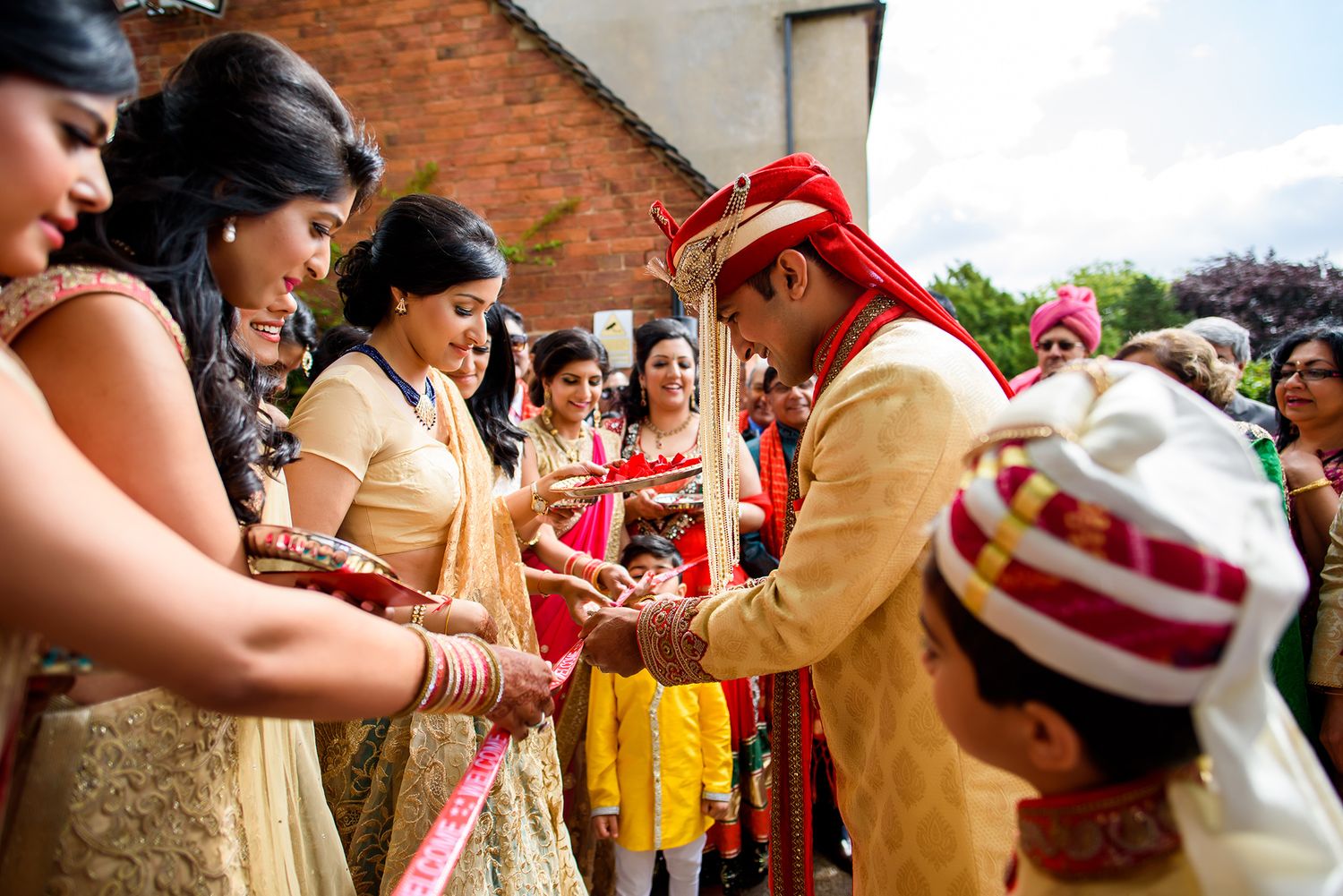 Traditional Indian wedding ceremony guests participate in ritual greetings and customs outside brick building.