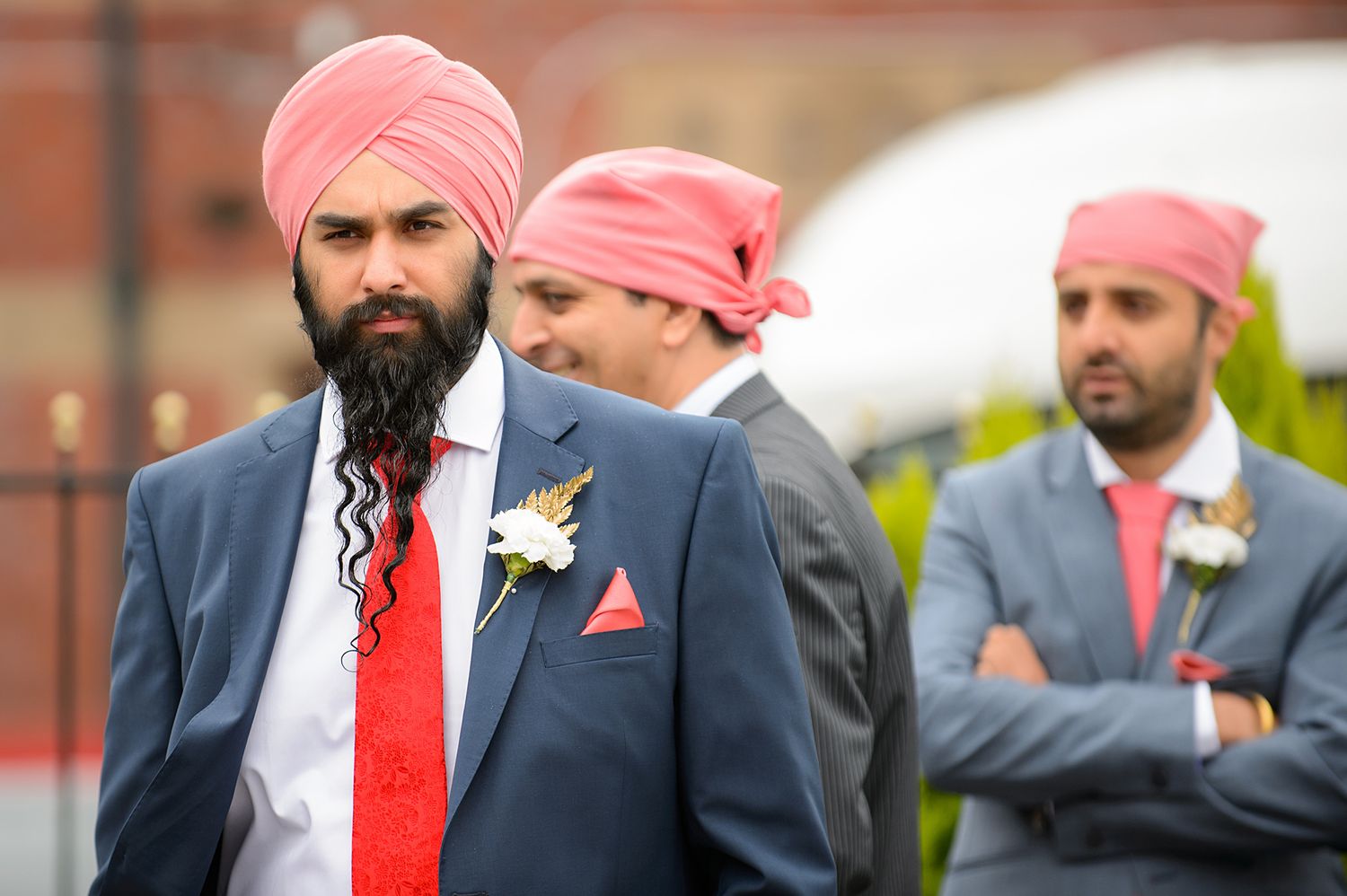 Groomsmen in navy suits and pink turbans stand together at an Indian wedding.