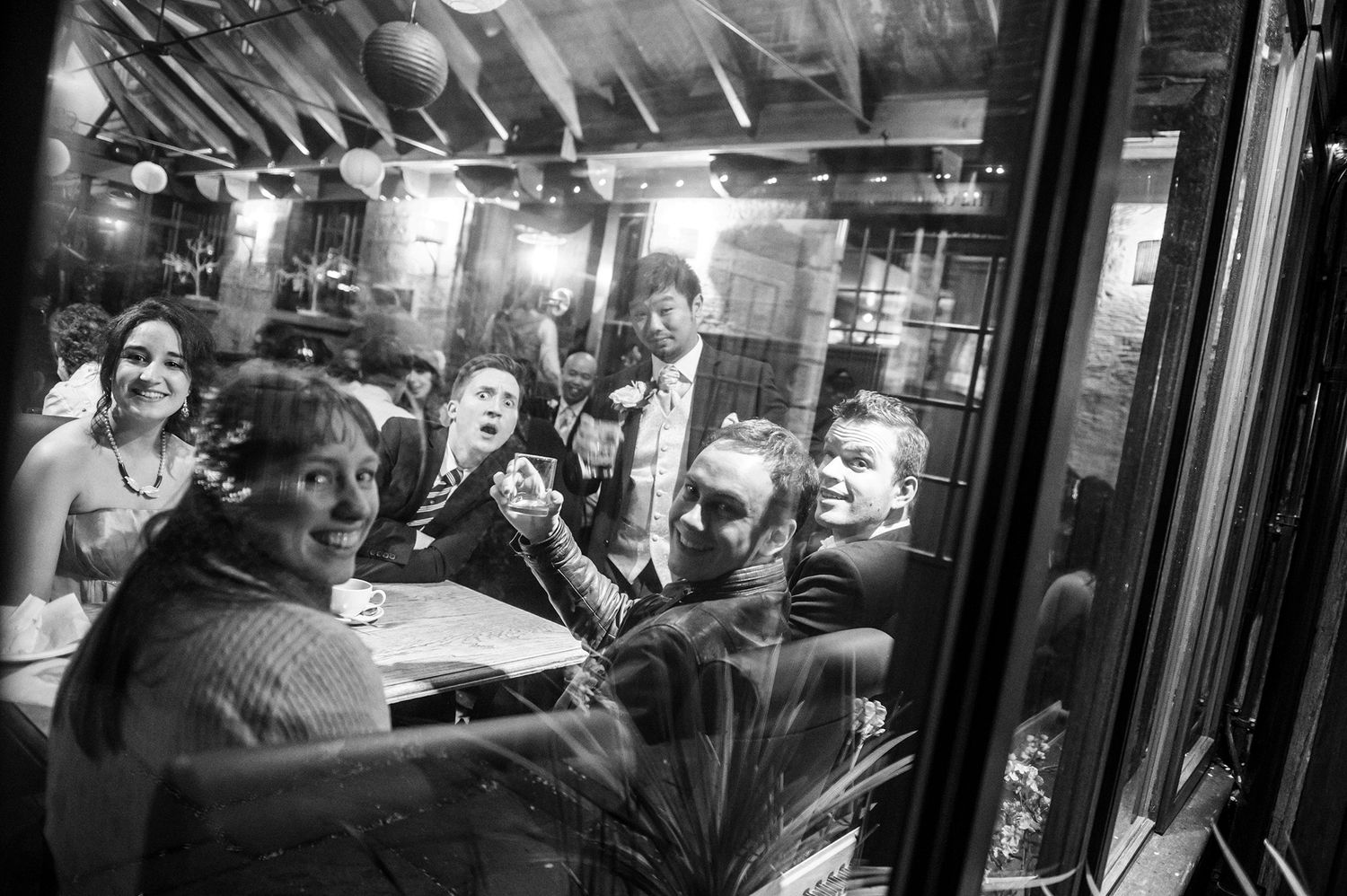 Evening celebration at venue with guests visible through large windows.