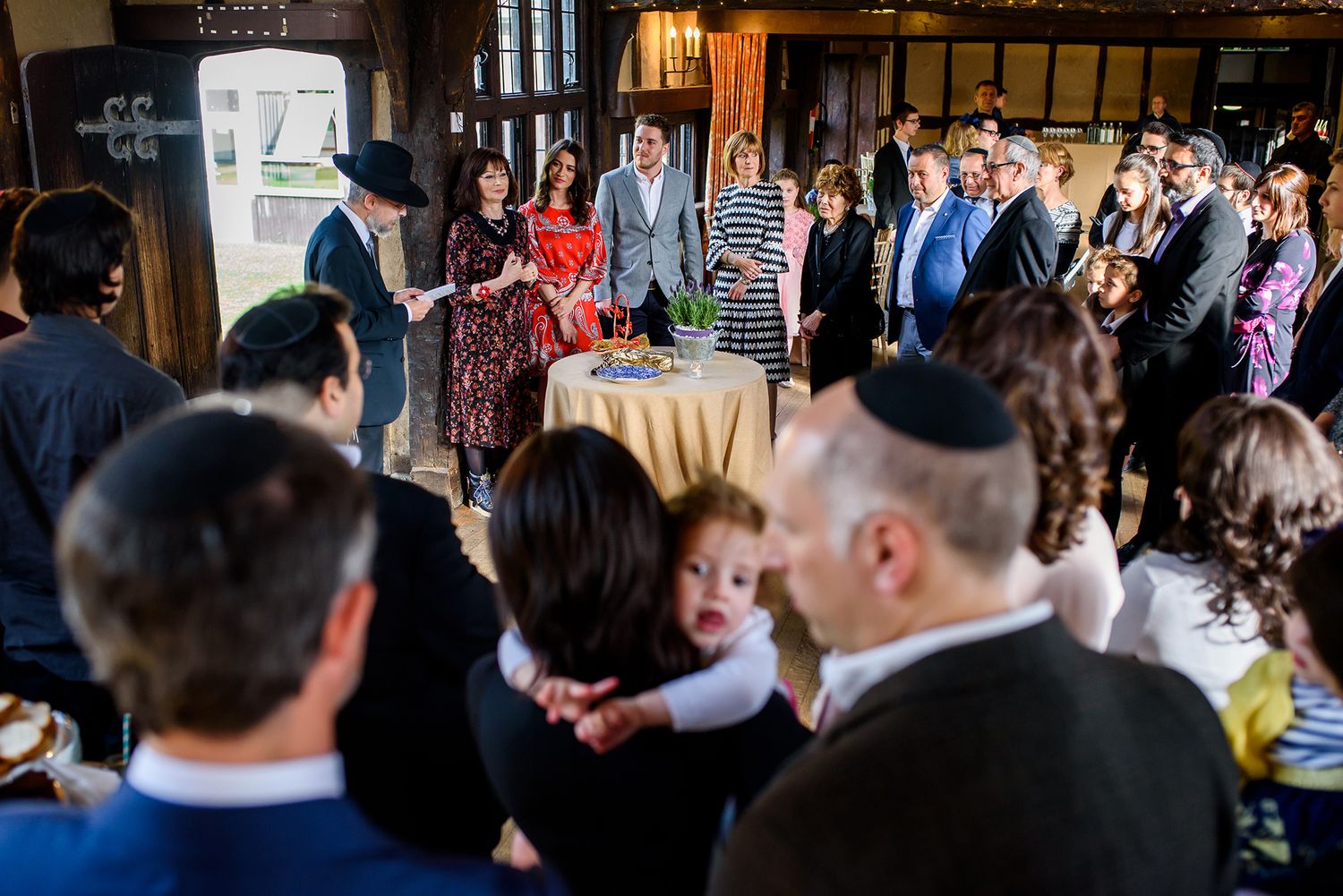 Wedding celebration with large crowd gathered in historic wood-beamed hall.