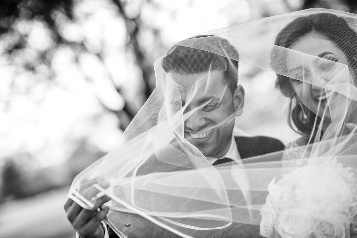 Black and white photo of a romantic wedding moment with flowing veil caught in the breeze.