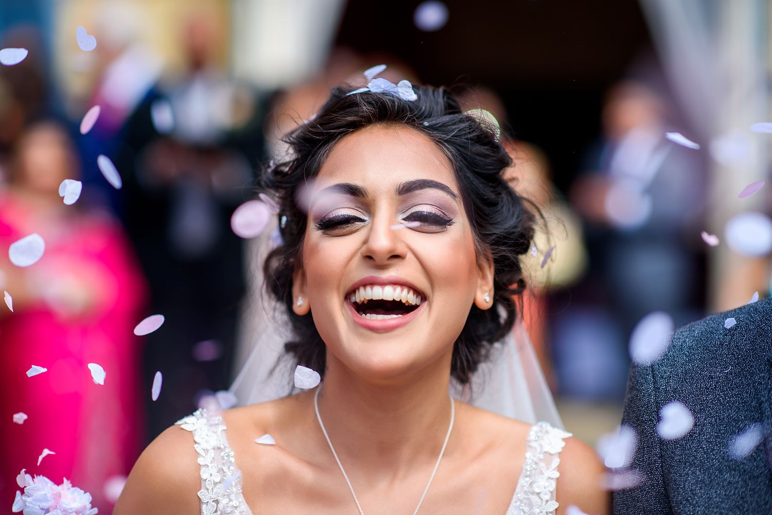 Joyful wedding celebration with guests throwing confetti and flower petals in the air with colorful bokeh lights.