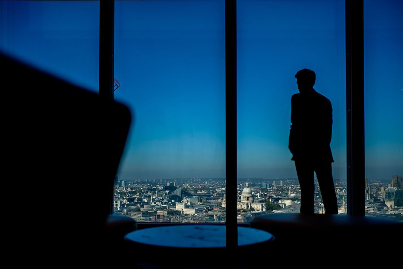 Silhouetted figures against large windows overlooking city skyline at dusk.
