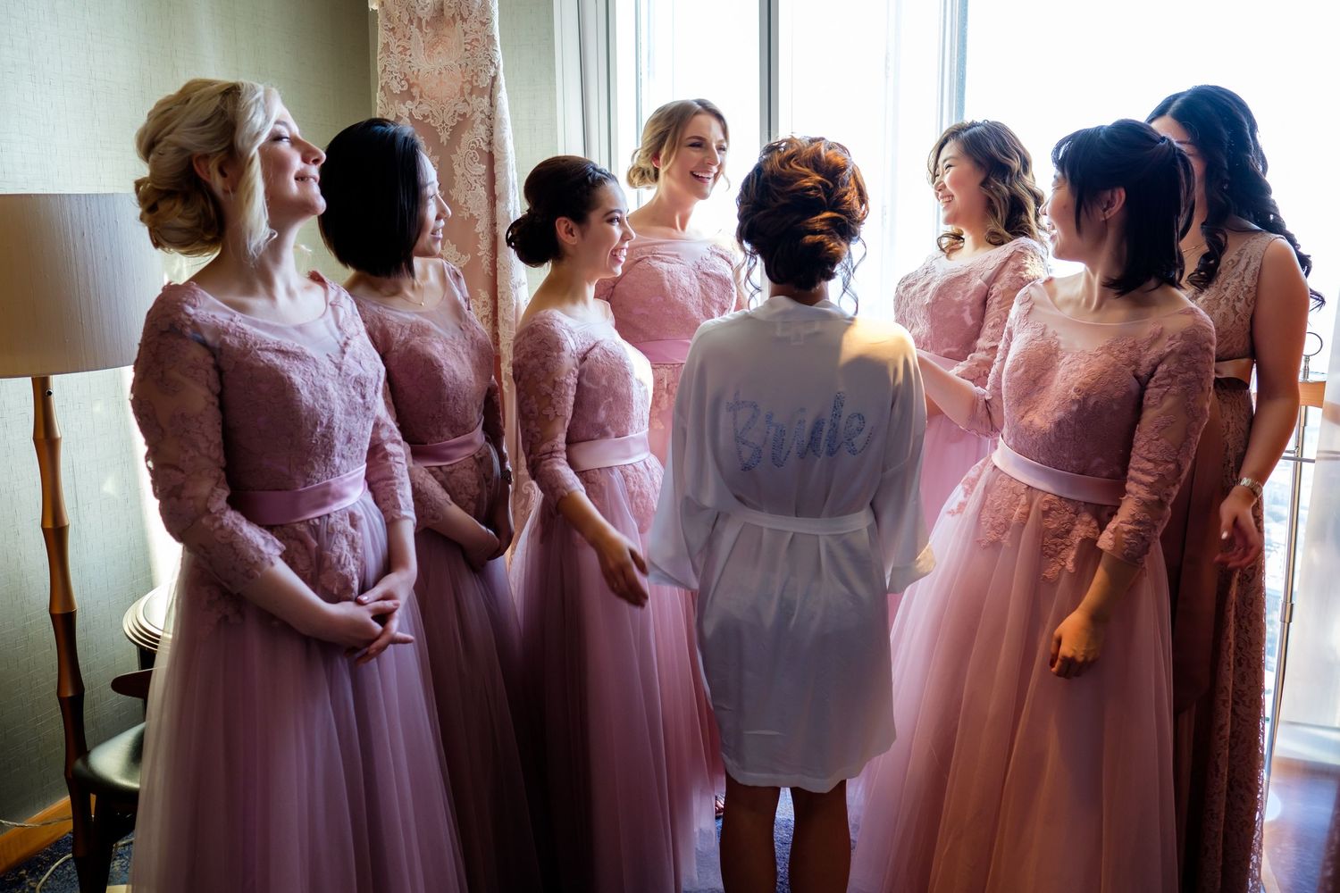 A row of bridesmaids in pink dresses stand together during a wedding celebration.