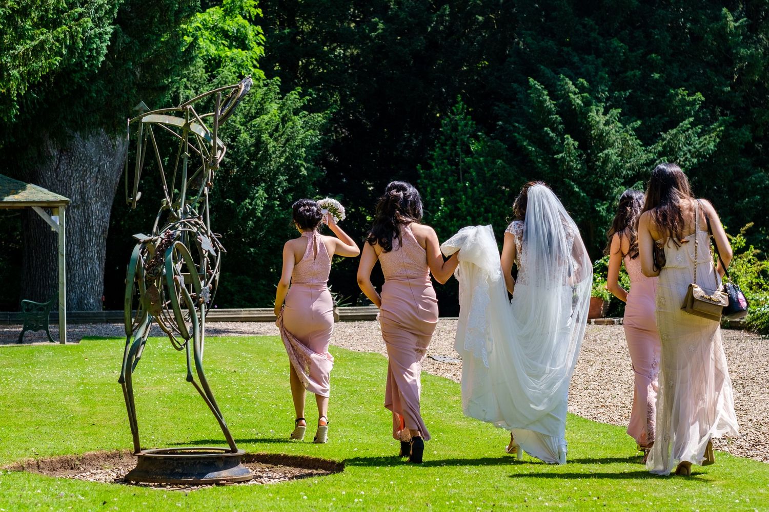 Bridesmaids in blush pink dresses walk together through a lush garden setting.