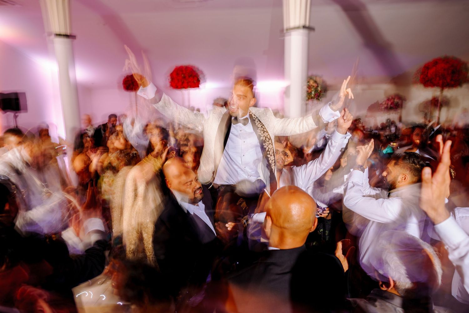 Wedding reception dance party with guests celebrating on the dance floor under pink and purple lighting.