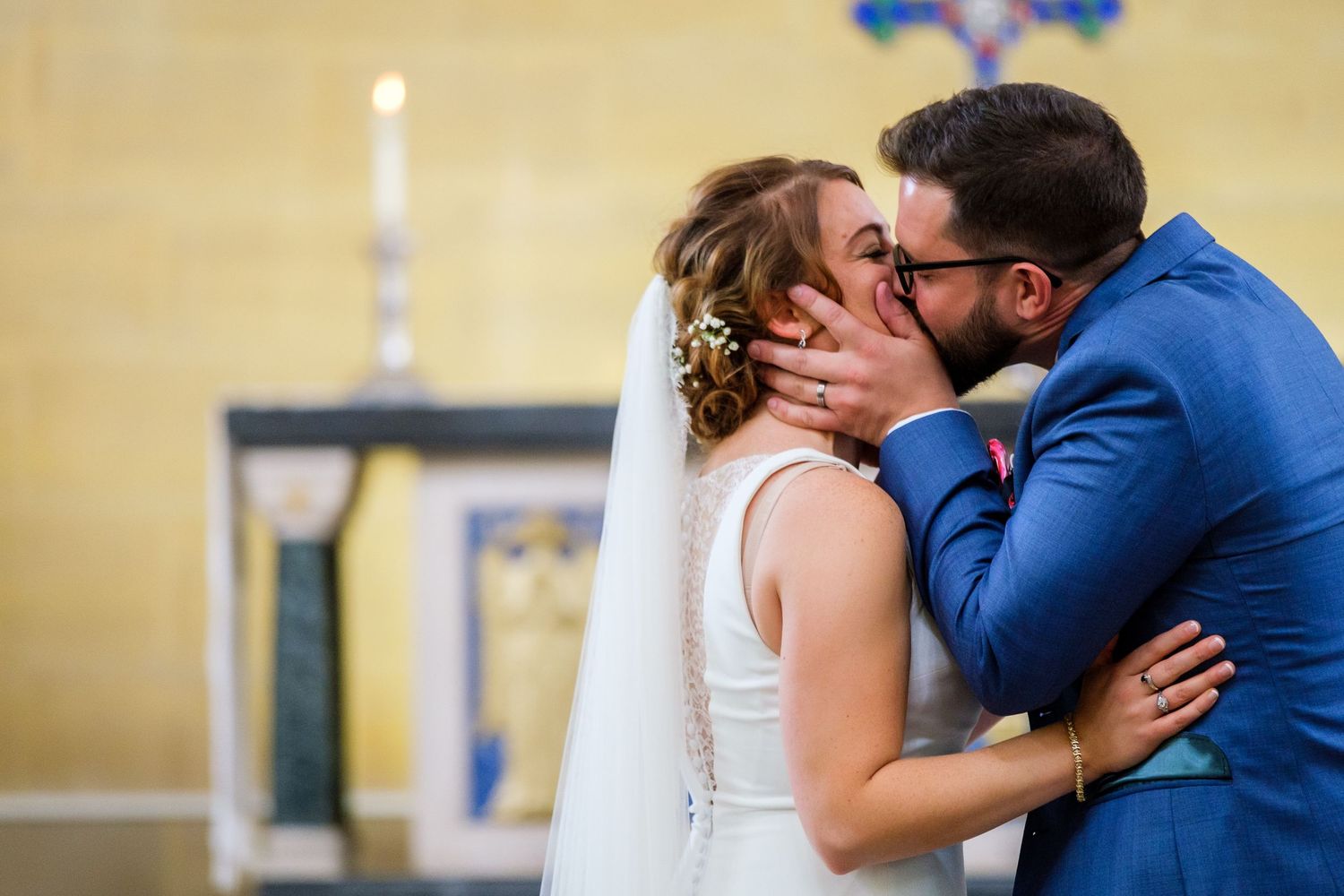 A romantic wedding kiss between a couple in a church with a yellow wall backdrop.