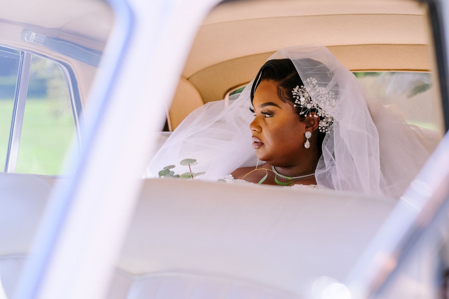 A bride wearing an elegant veil gazes out the window of a vintage car on her wedding day.