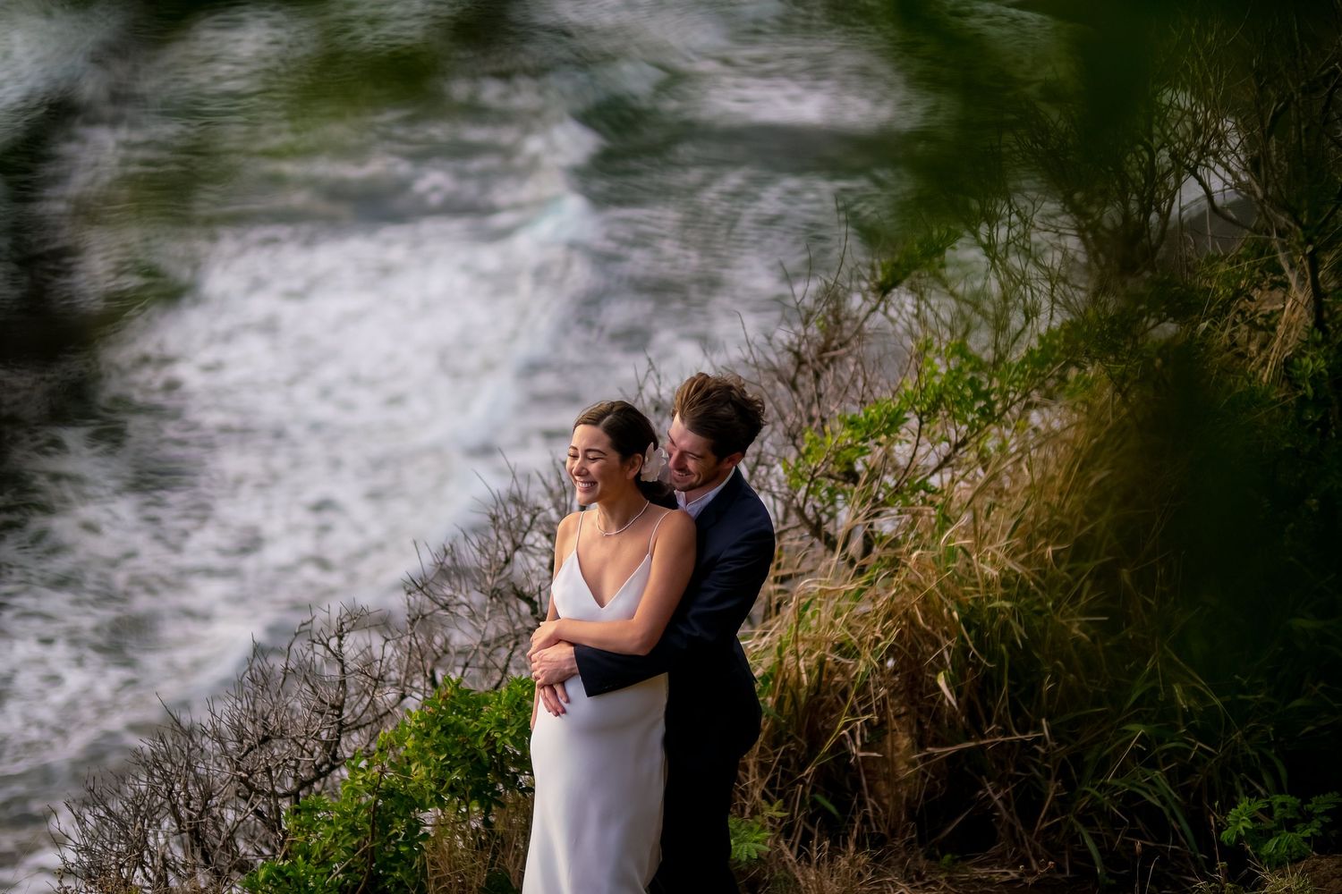 Ocean waves crash against rocks creating dramatic backdrop for romantic wedding photos.