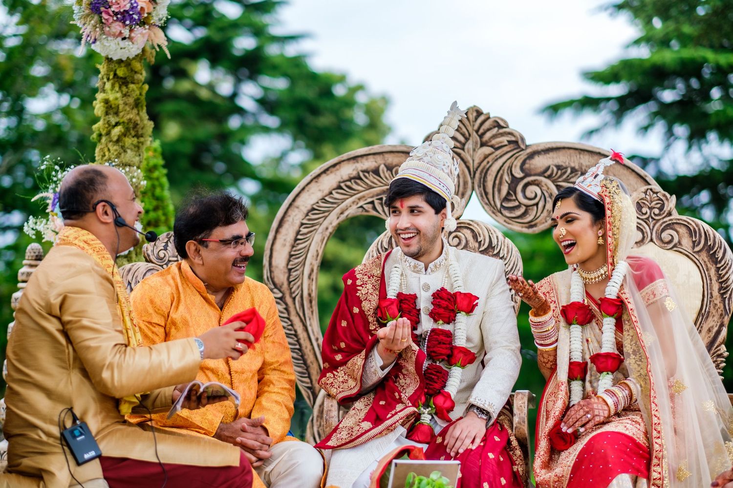 Traditional Indian wedding ceremony taking place outdoors with ornate carved backdrop and decorative elements.