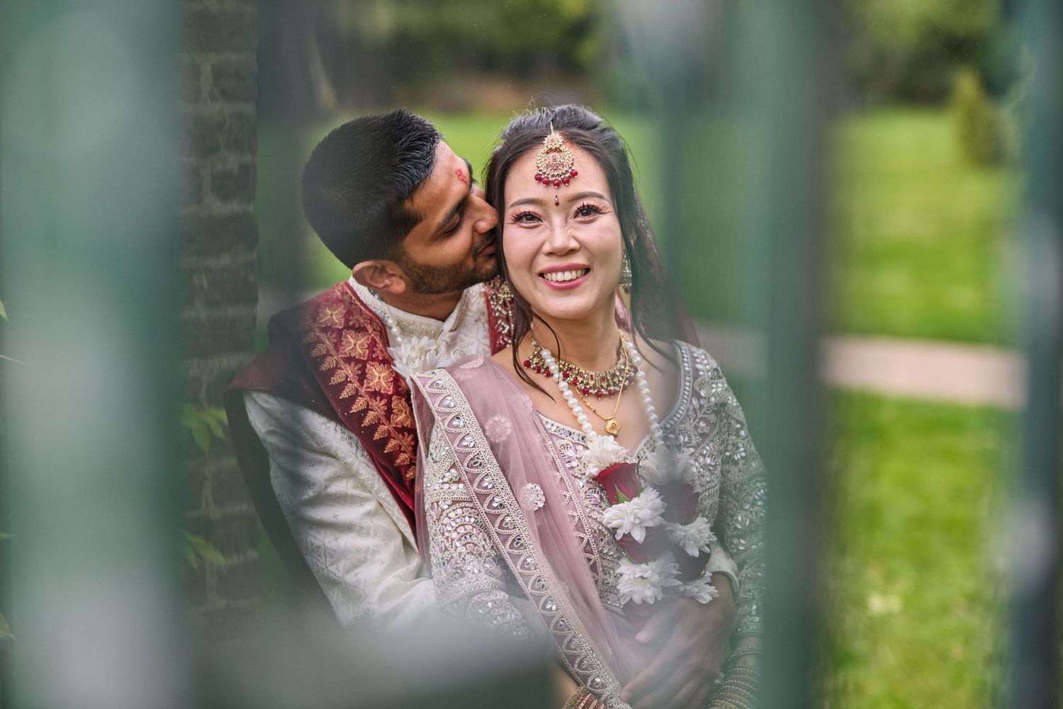 Romantic outdoor wedding portraits captured through garden greenery and architectural elements.