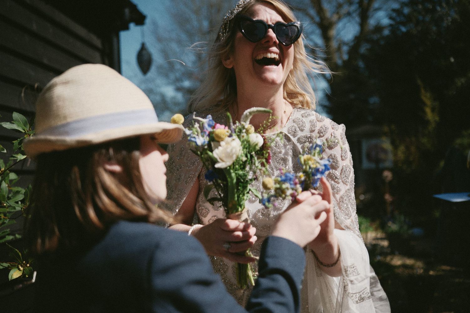 Sunlit outdoor wedding scene with laughter and white floral bouquets.